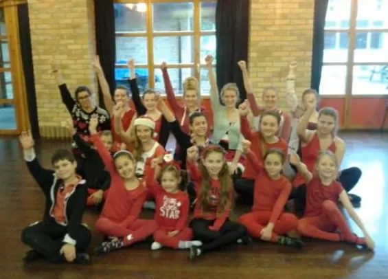 Large group of pupils in red costumes on stage in Harlow